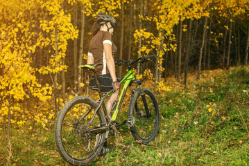 Woman biking in yellow autumn forest on a meadow