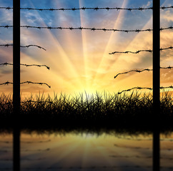 Silhouette of a broken border fence with barbed wire