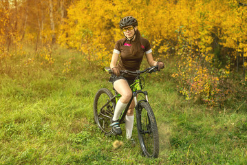 Woman biking in yellow autumn forest on a meadow