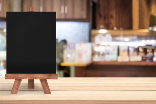 An empty blackboard with easel is on a wood table at a restauran