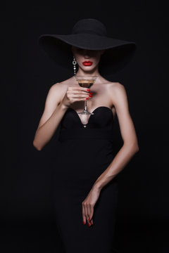 Luxury woman in a large black hat and bright lips with a glass of Martini.