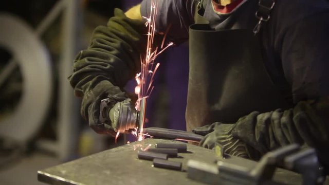 Shaky footage of a worker polishing some metal bar with a grinder, with sparks flying.