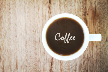 Inscription coffee in a cup of coffee and wooden background