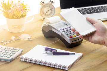 Hand holding mobile smart phone to made payment with credit card terminal or EDC. Customer pay by cellphone with empty screen.