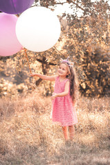 Cute baby girl 4-5 year old playing with balloons in park. Childhood.