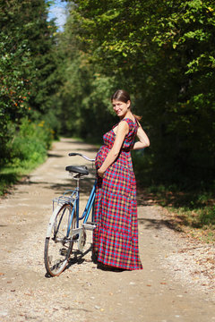 pregnant girl with bicycle on a forest road, rear view