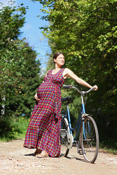 pregnant girl with bicycle on a forest road, front view
