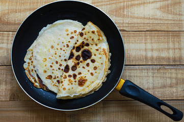 Top view of a frying pan with fresh homemade thin pancakes on wooden background