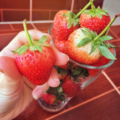 close up woman hand holding fresh strawberry with many strawberry in a glass at background