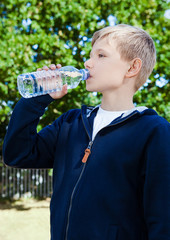 Young teenage boy drinking healthy still water in park