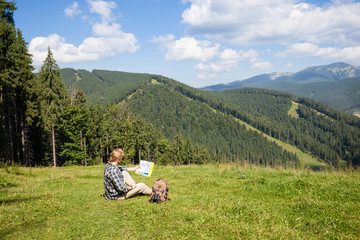 Fototapeta na wymiar Traveler sitting on the alpine meadow and looking at the map