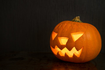 Halloween pumpkin with fire candle glowing on dark backdrop with reflection. Creepy face on halloween pumpkin from left side. 