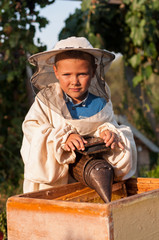 beekeeper portrait of a young boy who works in the apiary at hive with smoker for bees in hand
