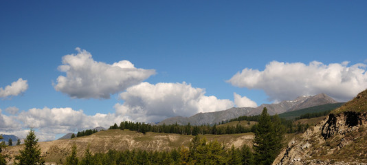 Blue sky and cumulus clouds over the Eastern Sayan Mountains and Mount MunKu-Sardyk. Photo partially tinted.