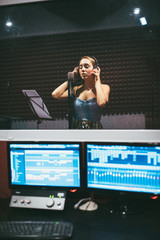 girl wearing headphones and singing into microphone in recording studio