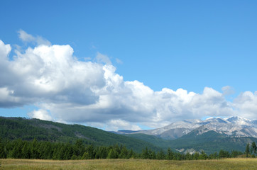 Blue sky and cumulus clouds over the Eastern Sayan Mountains and Mount MunKu-Sardyk. Photo partially tinted.
