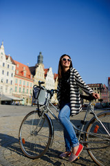 Fototapeta na wymiar The young brunette in sunglasses with bicycle in the center of the ancient city