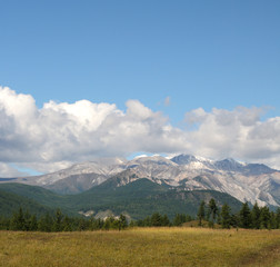 Blue sky and cumulus clouds over the Eastern Sayan Mountains and Mount MunKu-Sardyk. Photo partially tinted.