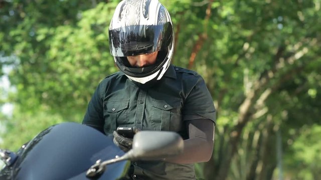 A man sitting on his motorcycle with his visor open looks at his phone as if seeking information about his whereabouts.
