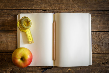 Apfel und Maßband liegen auf ein aufgeschlagenes Buch mit leeren Seiten