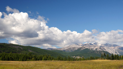 Blue sky and cumulus clouds over the Eastern Sayan Mountains and Mount MunKu-Sardyk. Photo partially tinted.