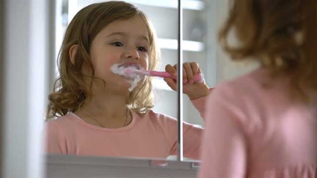 Little girl diligently brushing his teeth in the mirror.