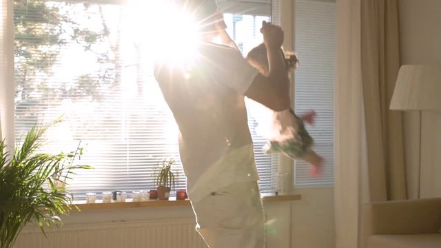 Dad turns and throws up a small daughter on hands in the Sunny living room. Slow motion.