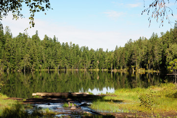 In the clear water of a forest lake reflects the sky, mountain, forest and clouds. Photo partially tinted.