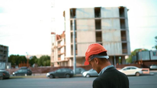 4k. UHD. Crane and beams. Rear view of young attractive architect looking digital pad and comparing housing construction project with building. Teal and orange middle steadicam shot.