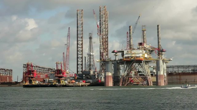 A speed boat races past several oil or gas drilling platforms in dry dock for repairs.