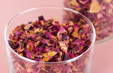 Rose petals in a glass bowl on rosy background. Dried blossoms, used for perfumes, cosmetics, teas and baths. Purple and orange colored organic herb. Isolated macro photo close up from above.
