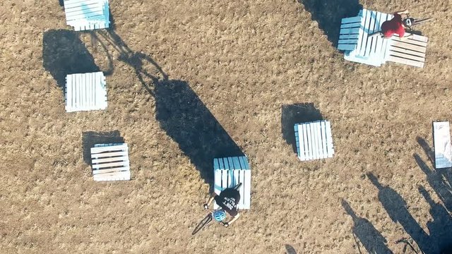 Сyclists doing jump MTB tricks in bicycle 4k aerial top view video. Mountain bike trial rider in park. Extreme sport lifestyle show