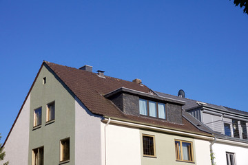 Fototapeta na wymiar House with dormer windows and tree on the top right corner against a blue sky