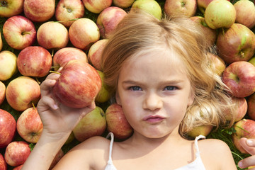 Portrait of child blond little cute girl lying on the grass with apples background
