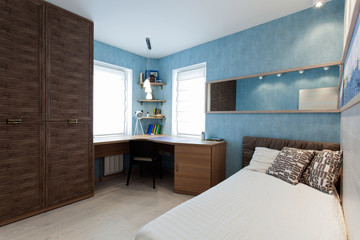Interior of a bedroom with a big cabinet, a writing desk, a bed, a mirror and  blue wallpaper