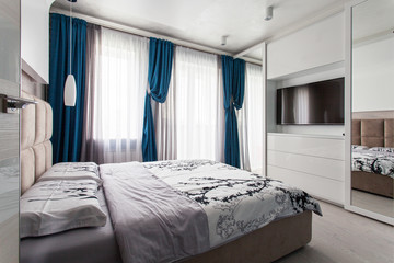 Design interior of a bedroom with a bed, big window, tv on the wall and mirrors