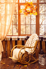 rocking-chair in the room with wooden walls, wicker wreath in autumn style hanging on the window