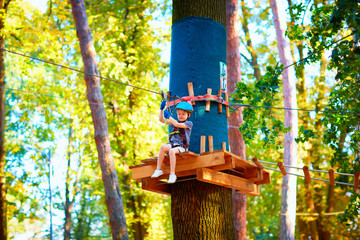 young boy passing the cable route high among trees, extreme sport in adventure park