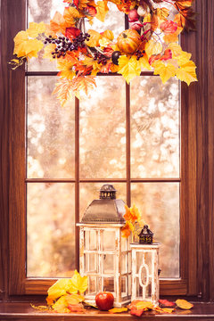 Autumn wreath with yellow leaves, berries, pumpkins, old lantern at the sunset window background