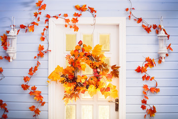 Autumn wreath entwined with leaves, garlic, berries, pumpkins, mushroom, hanging on the white door.