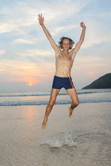 Man jumping happy on the beach with a sunset in the background