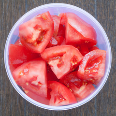 Fresh red tomato slice in plastic box on white wood table background