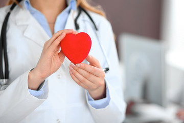 Female doctor with stethoscope holding heart.  Patients couple sitting in the background