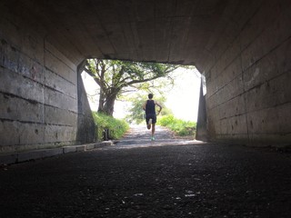 Runner exiting dark tunnel into summer light