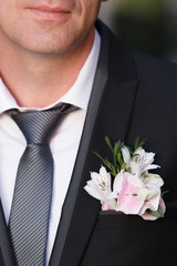 White and pink boutonniere on black suit of the groom