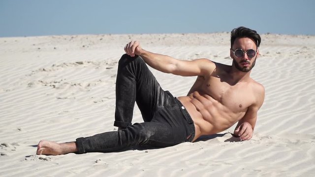 Beautiful guy sitting model looks and pours sand from hands