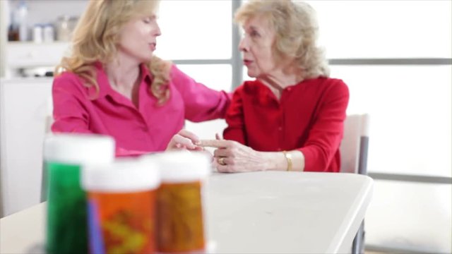 The camera rack focuses from prescription pill bottles in the foreground to a woman and her elderly mother talking.