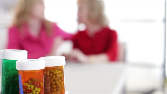 Focus is on prescription pill bottles with out of focus women talking in the background.