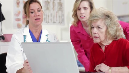 A pretty woman doctor using a laptop to show test results to an elderly patient and her daughter.