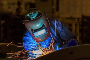 Welder with protective mask welding metal and sparks in car factory